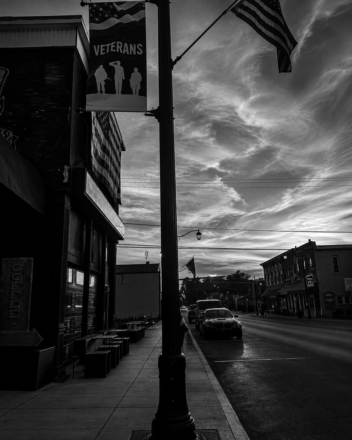 Main Street in Hagerstown, Indiana at dusk: a Thank You Veterans banner and American flags along the storefronts under a streaked evening sky